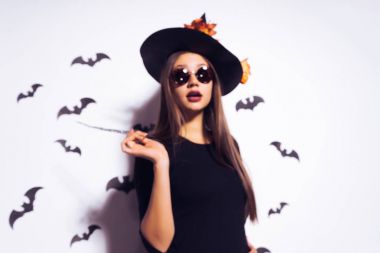 genç seksi Gotik kız bir cadı güneş gözlüğü ve büyük bir siyah şapka ayakta Halloween holding sihirli bir değnek için giyinmiş.
