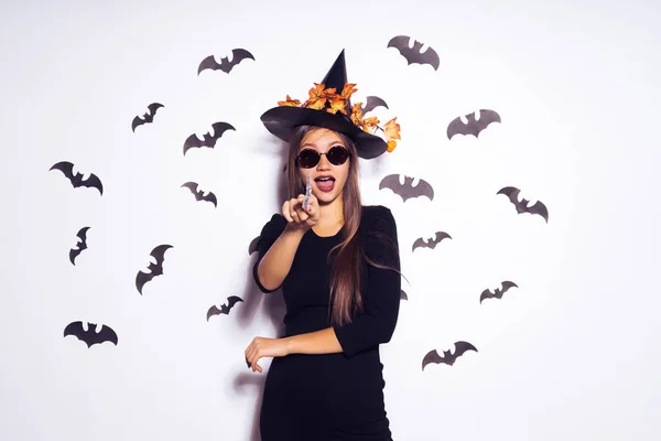 Giovane ragazza gotica sexy vestita con una strega per un Halloween, con un grande cappello nero e occhiali da sole, punta il dito contro la fotocamera — Foto Stock