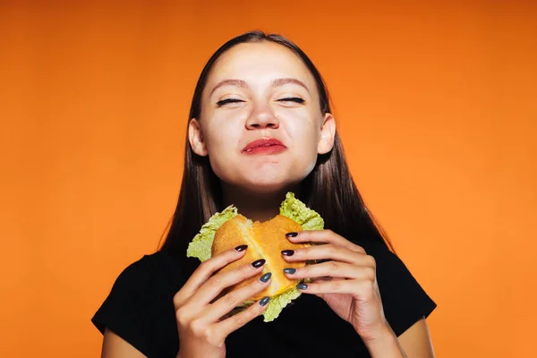 Молода красива дівчина хоче схуднути, але їсть великий шкідливий висококалорійний гамбургер — стокове фото