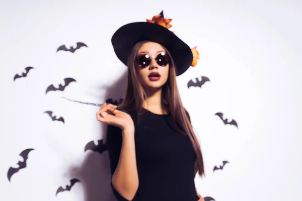 Sexy gothic meisje gekleed in een heks voor Halloween, permanent in zonnebrillen en een grote zwarte hoed, houden een toverstaf — Stockfoto