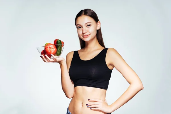 Güzel bir genç kız onun sağlık ve şekil, bir tabak yararlı sebze ve meyve ile tutarak izliyor — Stok fotoğraf