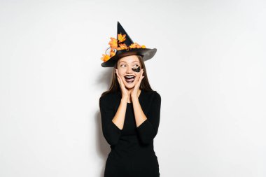 bir cadı Cadılar Bayramı, sarı yaprakları ile süslenmiş büyük bir siyah şapka ayakta için giyinmiş genç seksi Gotik kız güler