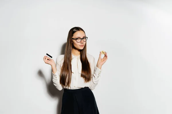 Una joven chica moderna y exitosa con gafas es la celebración de una tarjeta bancaria y bitcoin de oro — Foto de Stock