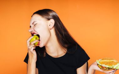 Hamburger diğer elinde bir elma ısırma tarafından tutan kız üzgün