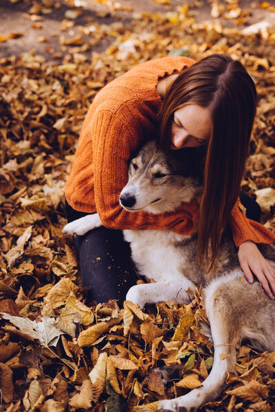 girl lies in a park in fallen leaves hugging her dog