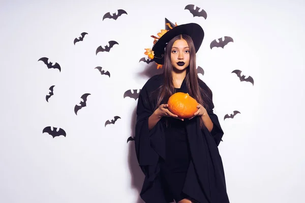 Chica en un traje de bruja sostiene una calabaza en sus manos — Foto de Stock
