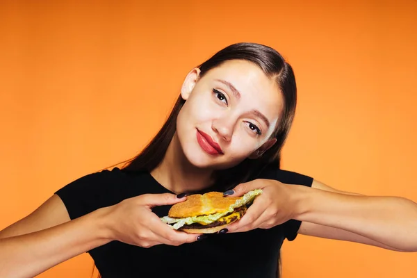 Fille heureuse tient soigneusement son hamburger sur un fond orange — Photo