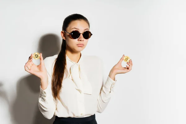 Una chica en redondo, gafas negras con un par de monedas-bitcoins en sus manos — Foto de Stock