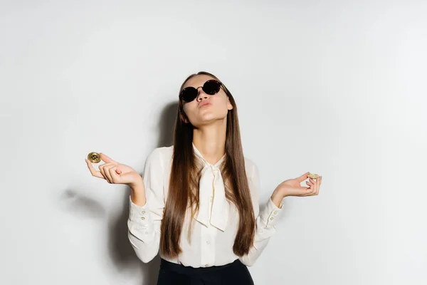 Una chica con gafas negras sostiene un par de bitcoins en sus manos — Foto de Stock