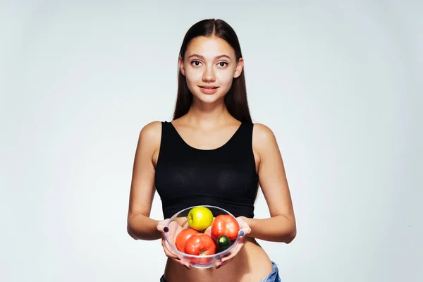 Menina em uniforme esportivo mantém uma tigela com legumes e maçãs — Fotografia de Stock