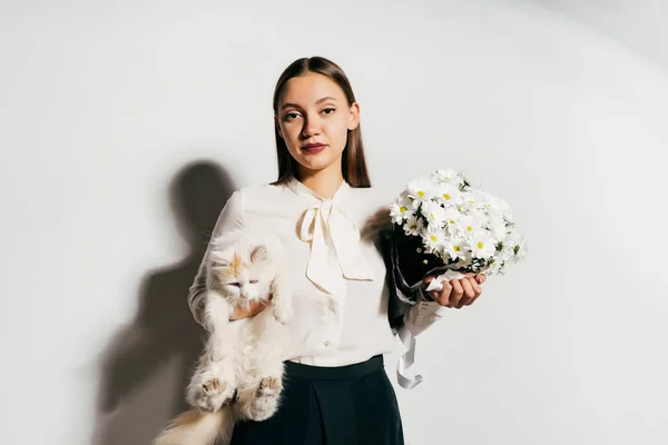 Menina chateada segurando um gato e um buquê de flores em suas mãos — Fotografia de Stock