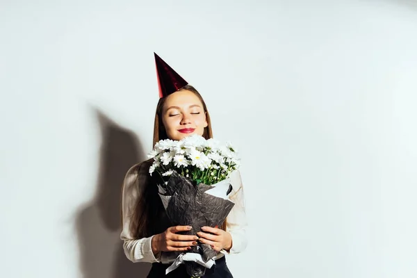 Flickan i en festlig mössa luktar en bukett blommor i händerna — Stockfoto