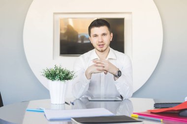genç adam beyaz gömlekli Office masada oturur ve kameraya benziyor