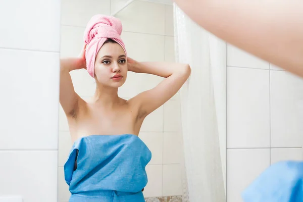 Süßes und schönes Mädchen nach der Dusche mit einem rosa Handtuch auf dem Kopf, das sich selbst im Spiegel betrachtet — Stockfoto