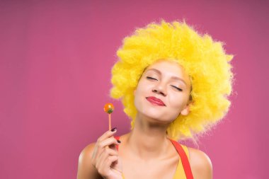 eğlenceli neşeli kız parlak sarı peruk çok renkli chupa chups kapalı gözleriyle yiyor.