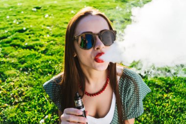 Mutlu moda gülümseyen kadın güneş gözlüğü vape Street, duman Sigara