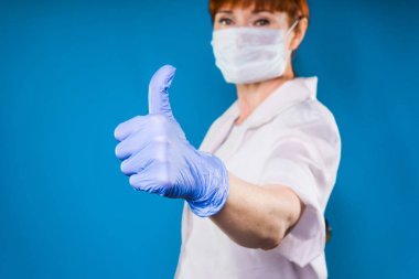 Hemşire maskeli başparmak yukarıya, izole üzerinde mavi arka plan gösterir