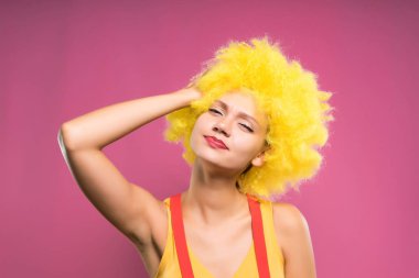 eğlenceli kamera, izole bir pembe, parlak sarı peruk neşeli kız bakar