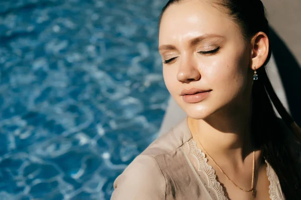 Девушка сидит у бассейна с закрытыми глазами и наслаждается теплым летним днем — стоковое фото