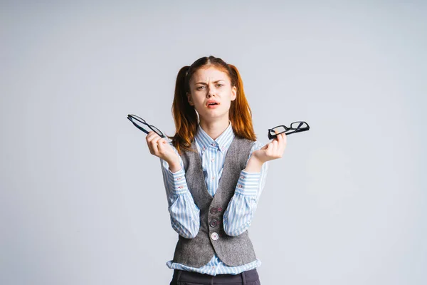 Ein müdes Mädchen mit zwei Schwänzen hält zwei Brillen in den Händen und weiß nicht, was sie wählen soll. isoliert. — Stockfoto