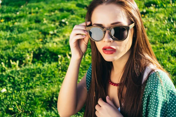 Giovane bella ragazza siede sul prato verde in occhiali da sole — Foto Stock