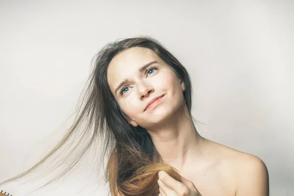 Ein junges schönes Mädchen berührt ihr langes Haar, schaut verträumt irgendwohin — Stockfoto