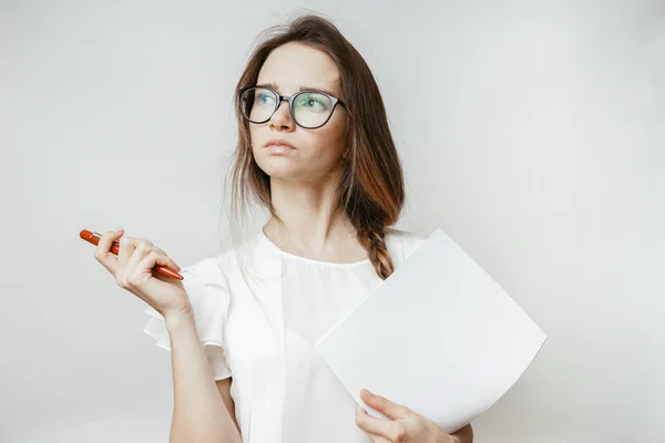 Junges schönes Mädchen mit Brille denkt über etwas nach, hält Papier und Stift in der Hand — Stockfoto