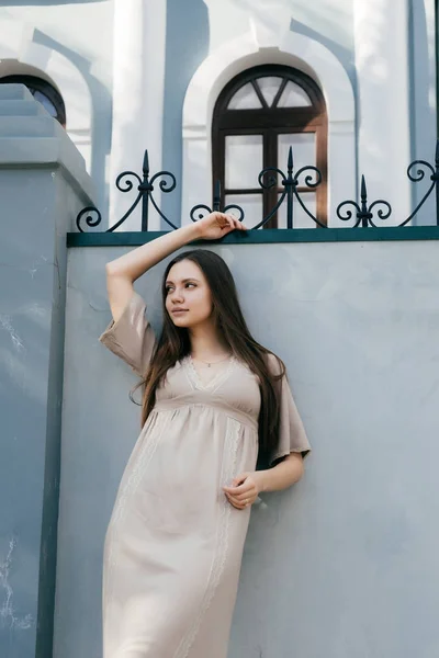 Jovem menina bonita em um vestido bege posando contra uma parede cinza — Fotografia de Stock