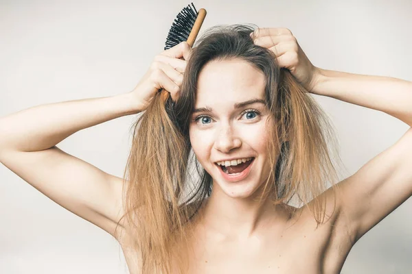 Jeune fille drôle s'amuser, en essayant de peigner ses cheveux blonds avec un peigne en bois — Photo