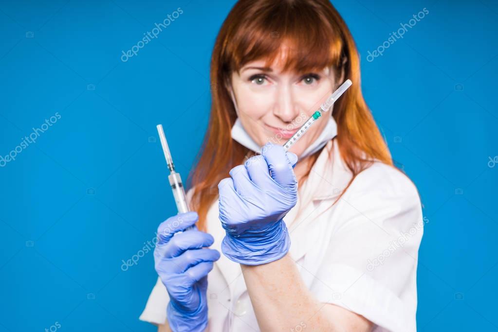 adult red-haired woman doctor holding syringes, smiling