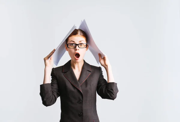 Молодая успешная деловая женщина в очках и строгом офисном костюме держит важные бумаги и выглядит удивленной — стоковое фото