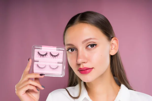 Junges schönes Mädchen mit einem Paket mit schwarzen falschen Wimpern in ihren Händen — Stockfoto