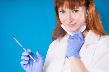 Yetişkin Kızıl saçlı kadın doktor beyaz laboratuar ceket ve mavi medikal eldiven şırınga tutar