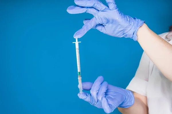 Un médico con una bata de laboratorio blanca y guantes médicos azules sostiene una jeringa — Foto de Stock