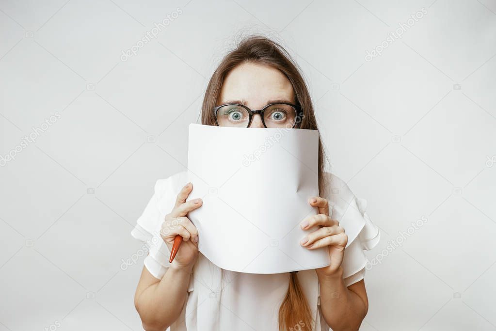 a young cute girl with glasses covers half of her face with a sheet of white paper