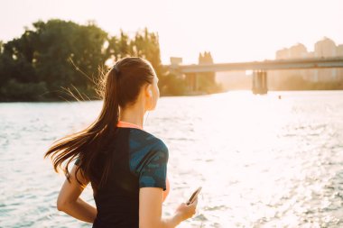 ırmak kenarına, gün batımında genç modern kız ishal dinler kulaklık müzik
