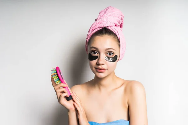 Młoda, piękna dziewczyna z różowy ręcznik na głowie, silikon czarny plastry pod oczy trzymając w ręku grzebień — Zdjęcie stockowe
