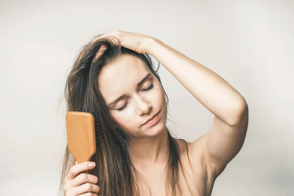 Jovem menina de cabelos longos penteia o cabelo com um pente de madeira — Fotografia de Stock