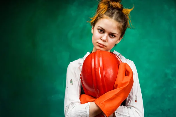 Mooie meisje in oranje rubberen handschoenen houdt een beschermende helm in handen — Stockfoto