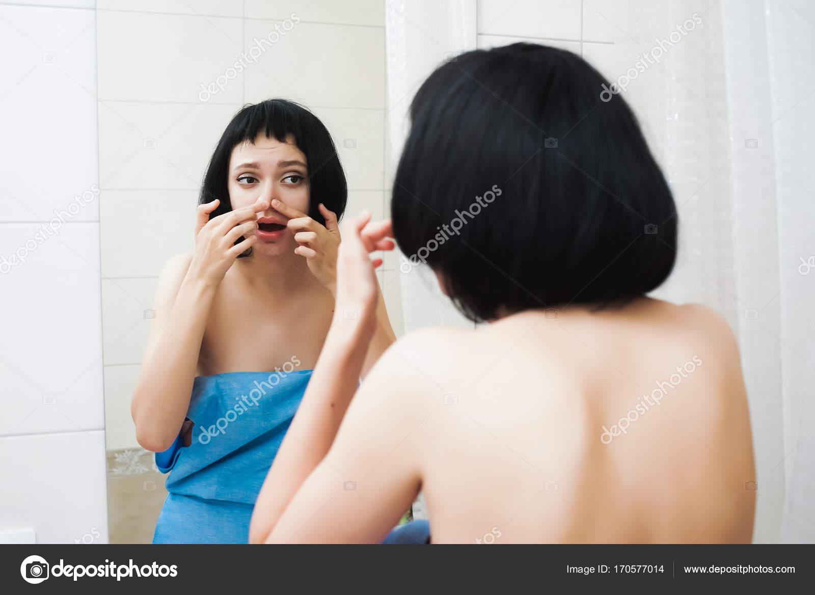 A young beautiful girl with black short hair stands at the mirror in a blue  towel and wants to squeeze out black dots on the nose Stock Photo by  ©mne_len 170577014
