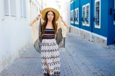 genç güzel kız eğleniyor, Dil Gösterilen, bir hasır şapka giymiş, eski şehir Arnavut kaldırımlı bir yol boyunca yürüyüş