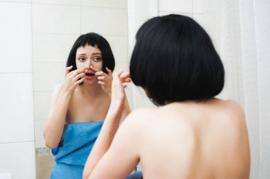 siyah kısa saçlı güzel bir genç kız mavi havlu aynada, anlamına gelir ve burun üzerindeki siyah noktalar dışarı sıkmak istiyor