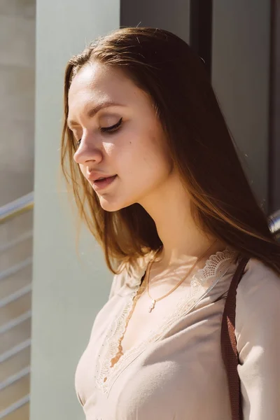 Giovane bella ragazza in un abito beige sta al sole e guarda giù — Foto Stock