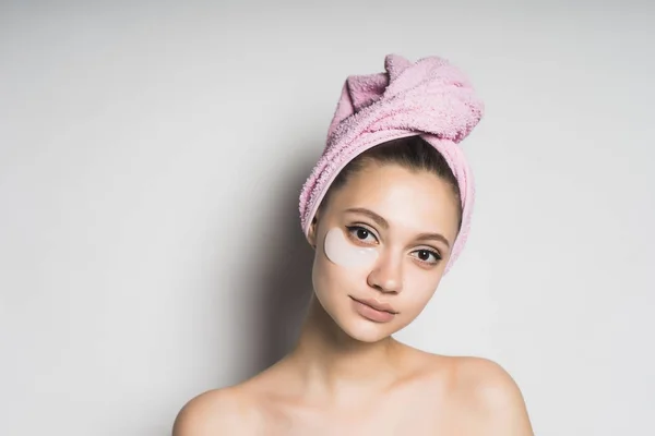 Jovem menina bonita com pele limpa com uma toalha rosa na cabeça e manchas de silicone sob os olhos, sorrindo — Fotografia de Stock