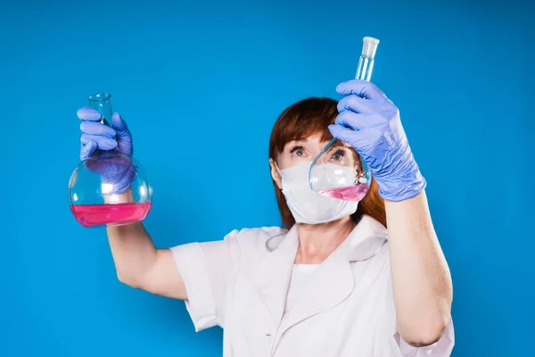 의료 보호 마스크와 흰 가운에 성인 여성 의사 보유 플라스 크 내부 화학 솔루션 — 스톡 사진