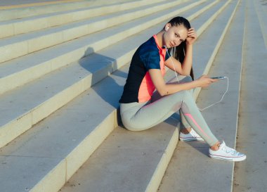 kulaklıklar müzik dinlemek güneşte merdivenlerde oturan genç sportif kız