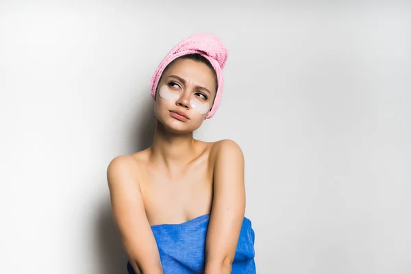 Молодая красивая девушка с розовым полотенцем на голове и силиконовыми пятнами под глазами, задумчиво глядя куда-то — стоковое фото
