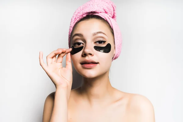 Jovem menina bonita com uma toalha rosa na cabeça e manchas de silicone preto sob os olhos, sorrindo — Fotografia de Stock