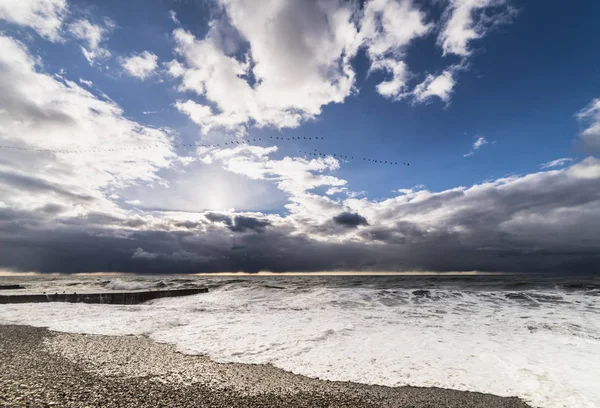 The raging waves are washed by a stone beach against a blue sky with white clouds — Stock Photo, Image