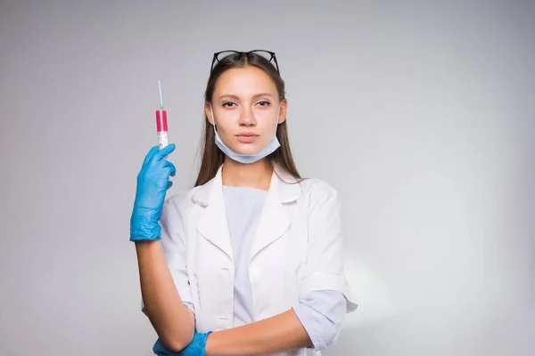 Giovane ragazza in cappotto bianco medico e maschera che indossa occhiali in mano tenendo una siringa medica — Foto Stock